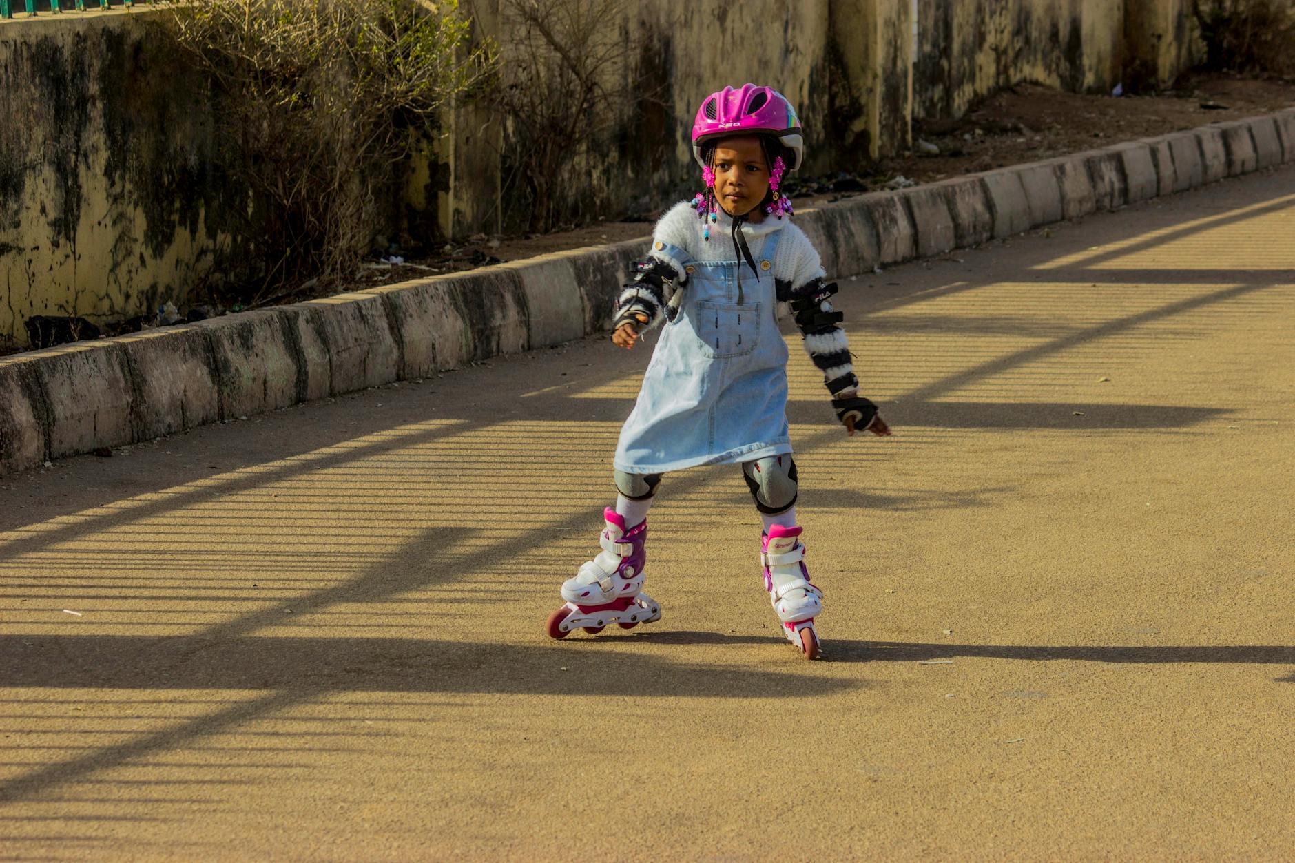Dziewczynka w kasku i ochraniaczach uczy się jeździć na rolkach