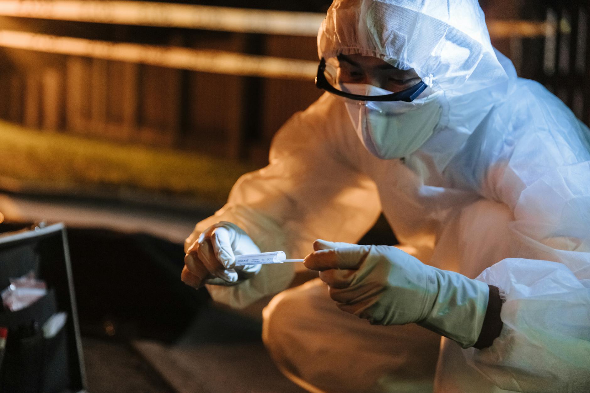 Biegły w kombinezonie zabezpiecza ślady na miejscu zbrodni nocą