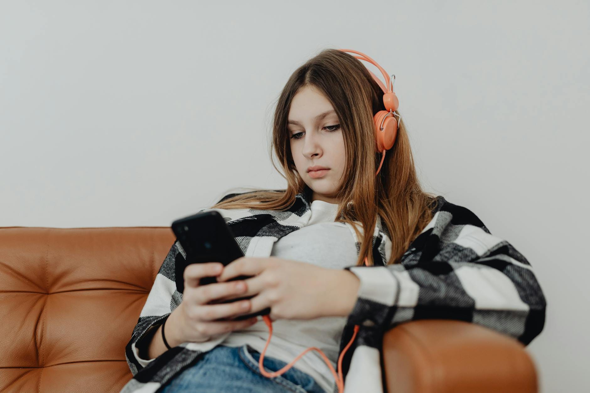 Nastolatka na kanapie ze słuchawkami, patrzy w smartfon